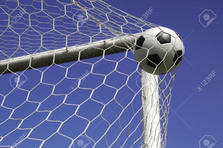 soccer ball (football) in corner of the goal with a blue sky background.