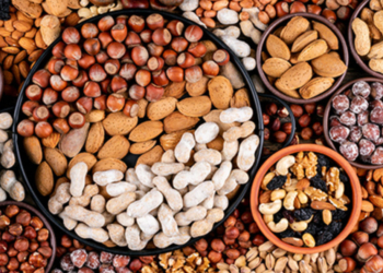 Some of assorted nuts and dried fruits with pecan, pistachios, almond, peanut, cashew, pine nuts in a different bowls and black pan flat lay.