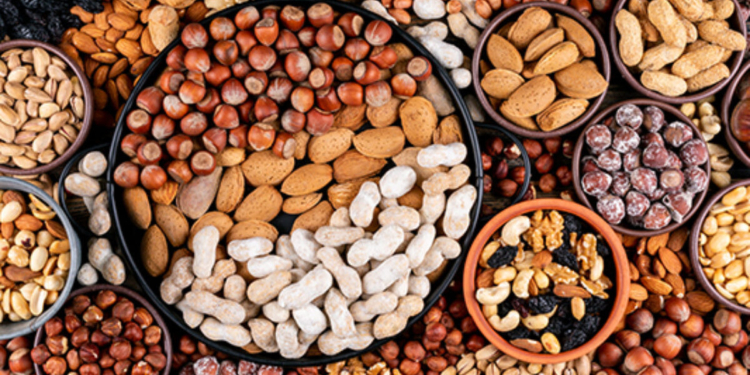 Some of assorted nuts and dried fruits with pecan, pistachios, almond, peanut, cashew, pine nuts in a different bowls and black pan flat lay.
